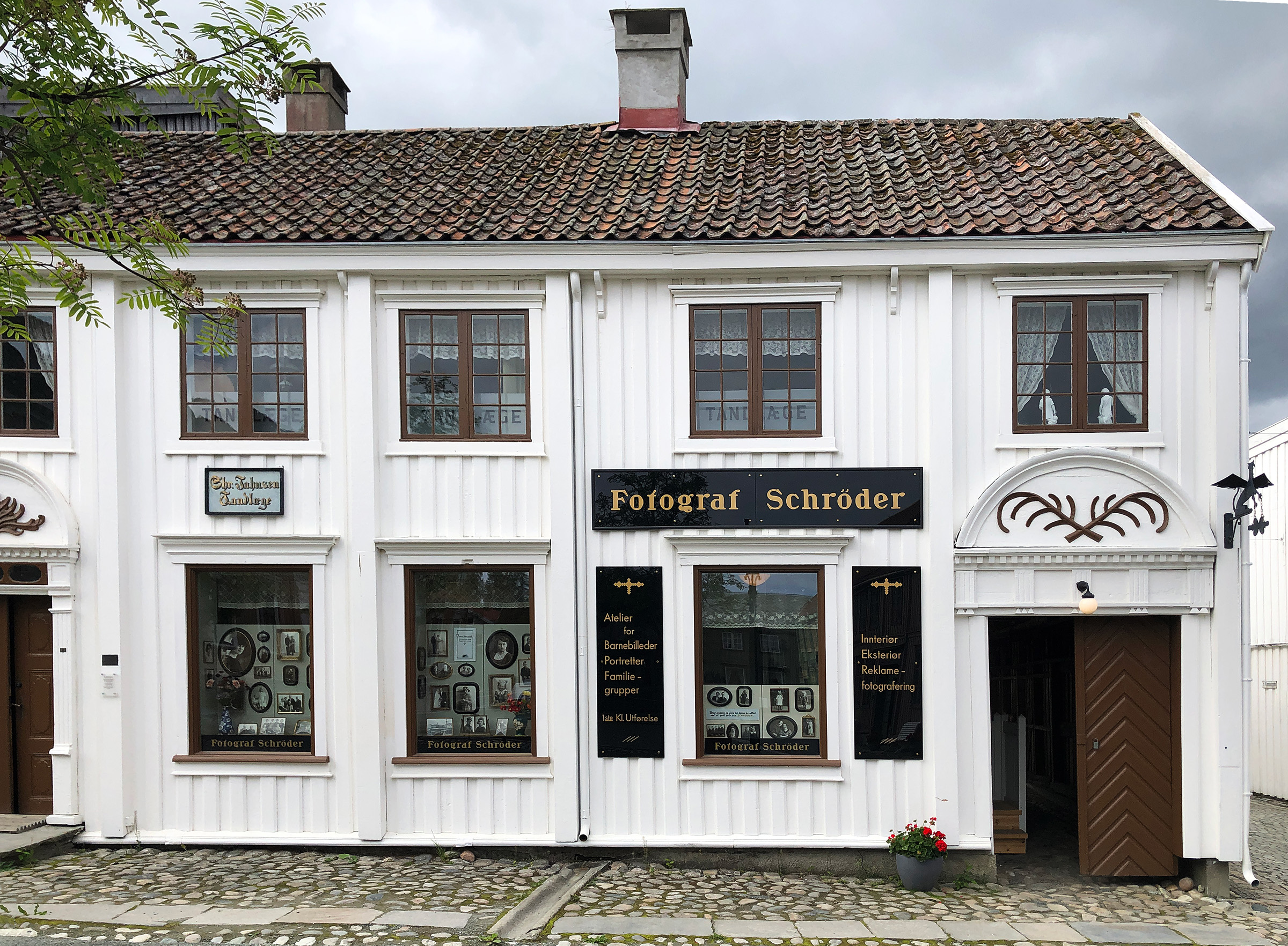 Foto av hvitt, gammelt hus med fasadeskilt for Fotograf Schrøder